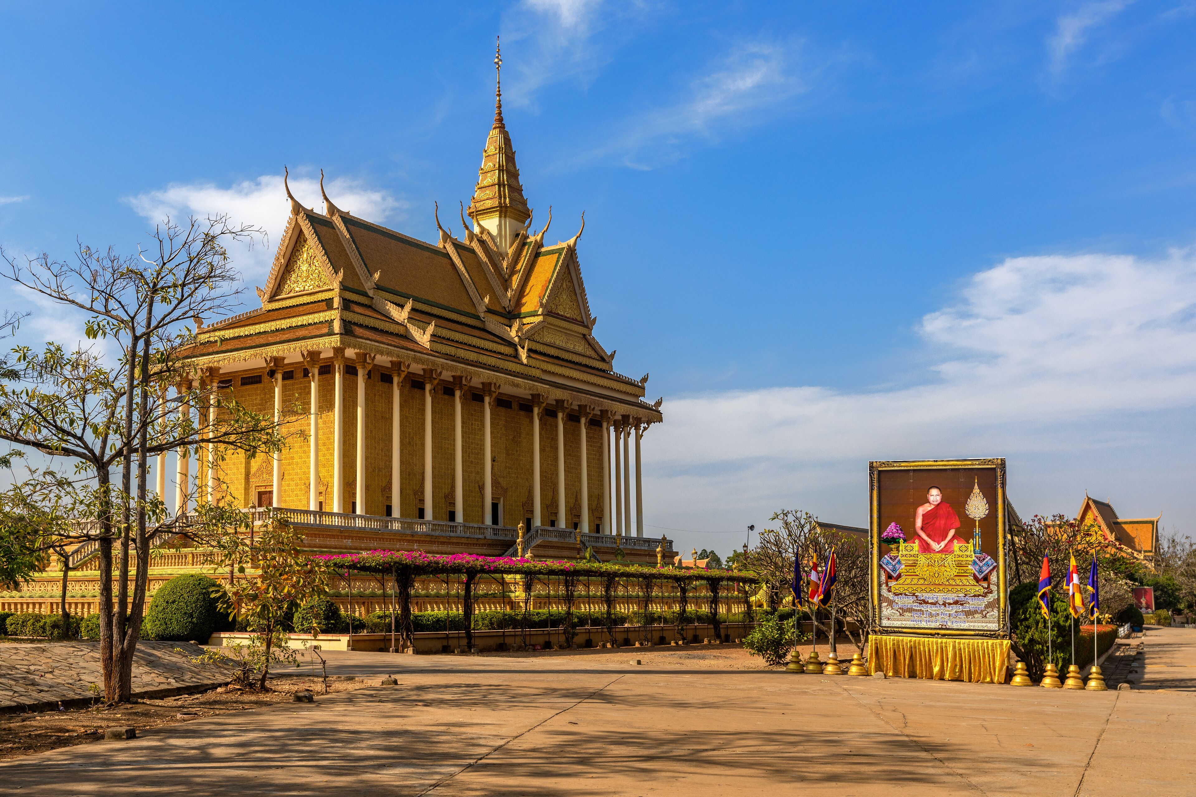 A traditional Thai temple with a golden spire, a large Buddha statue, and a well-maintained garden.