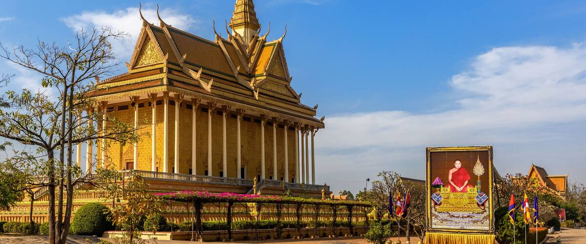A traditional Thai temple with a golden spire, a large Buddha statue, and a well-maintained garden.