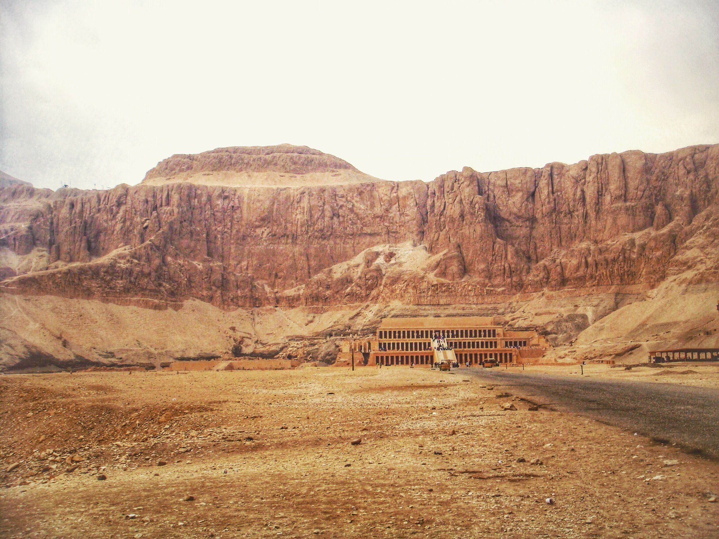 A desert landscape with a large building and a road leading towards it.