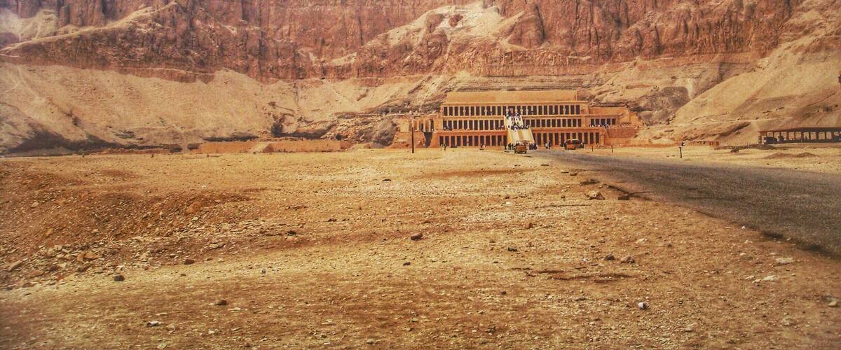 A desert landscape with a large building and a road leading towards it.