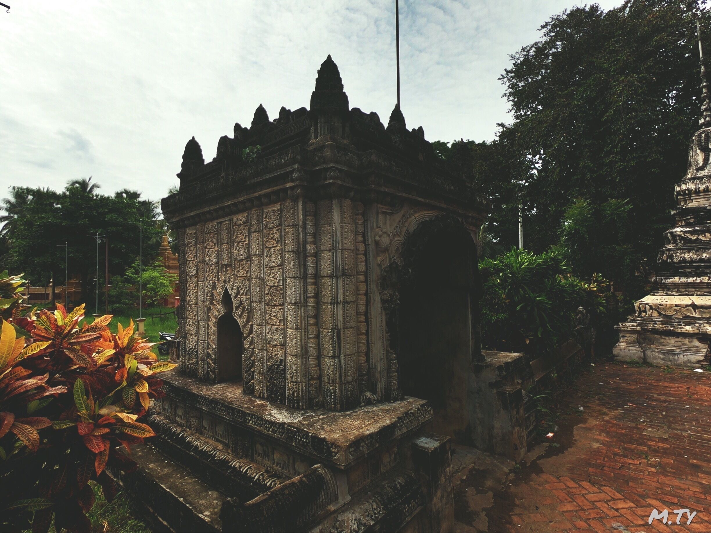 An ancient stone structure with intricate carvings and a statue in a lush garden.