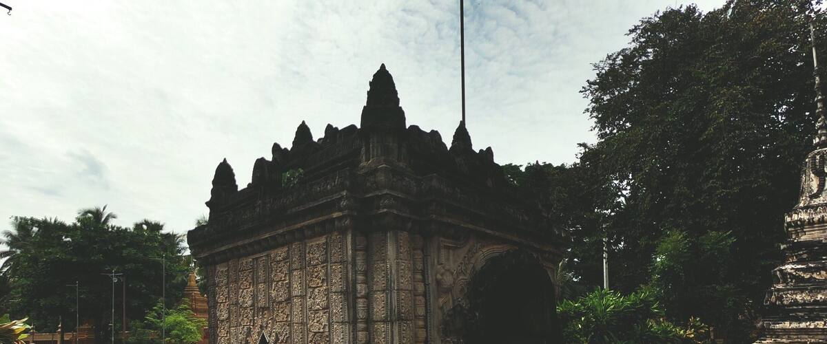 An ancient stone structure with intricate carvings and a statue in a lush garden.