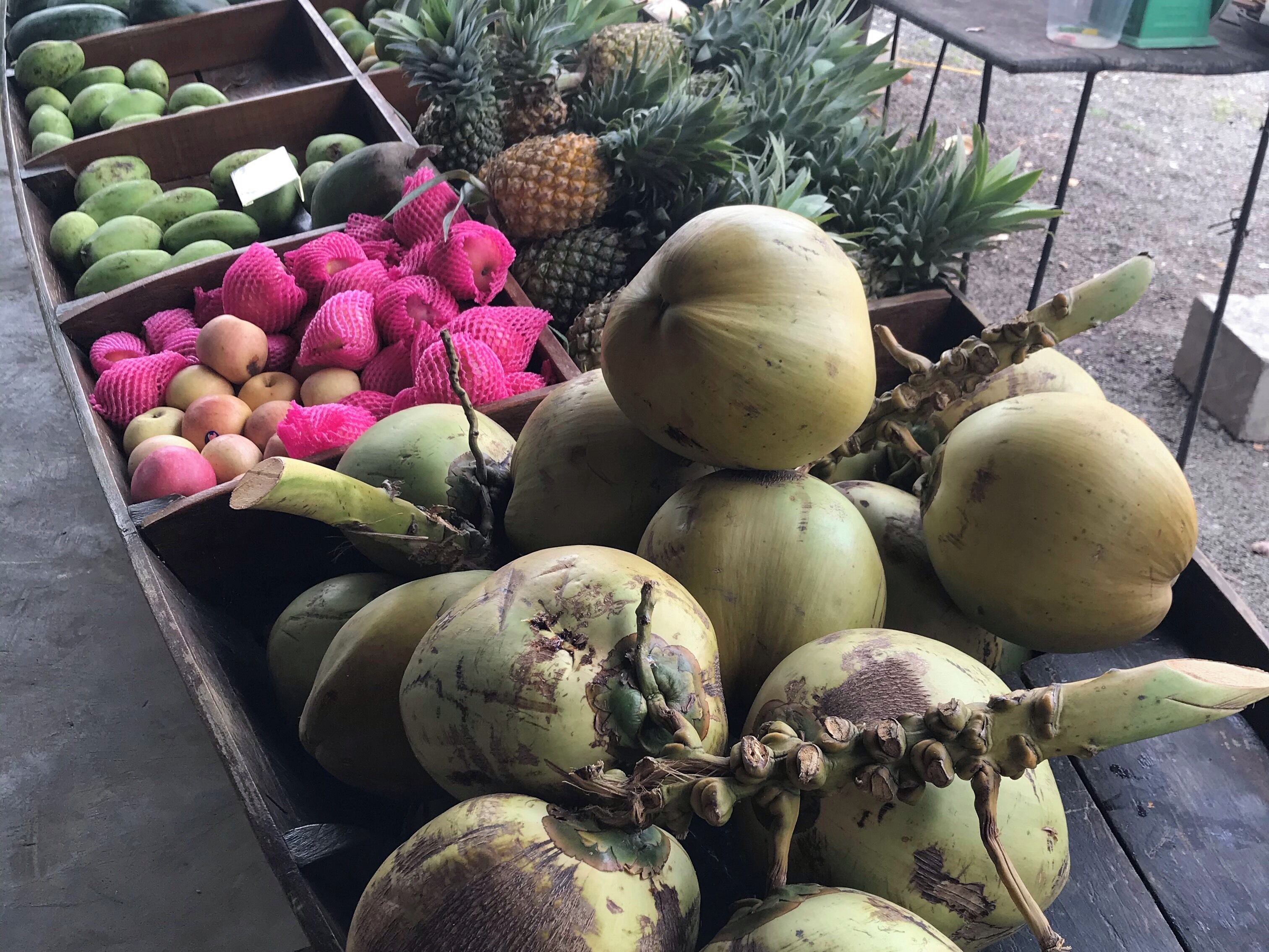 A fruit stand with various fruits including mangoes, pineapples, and coconuts.