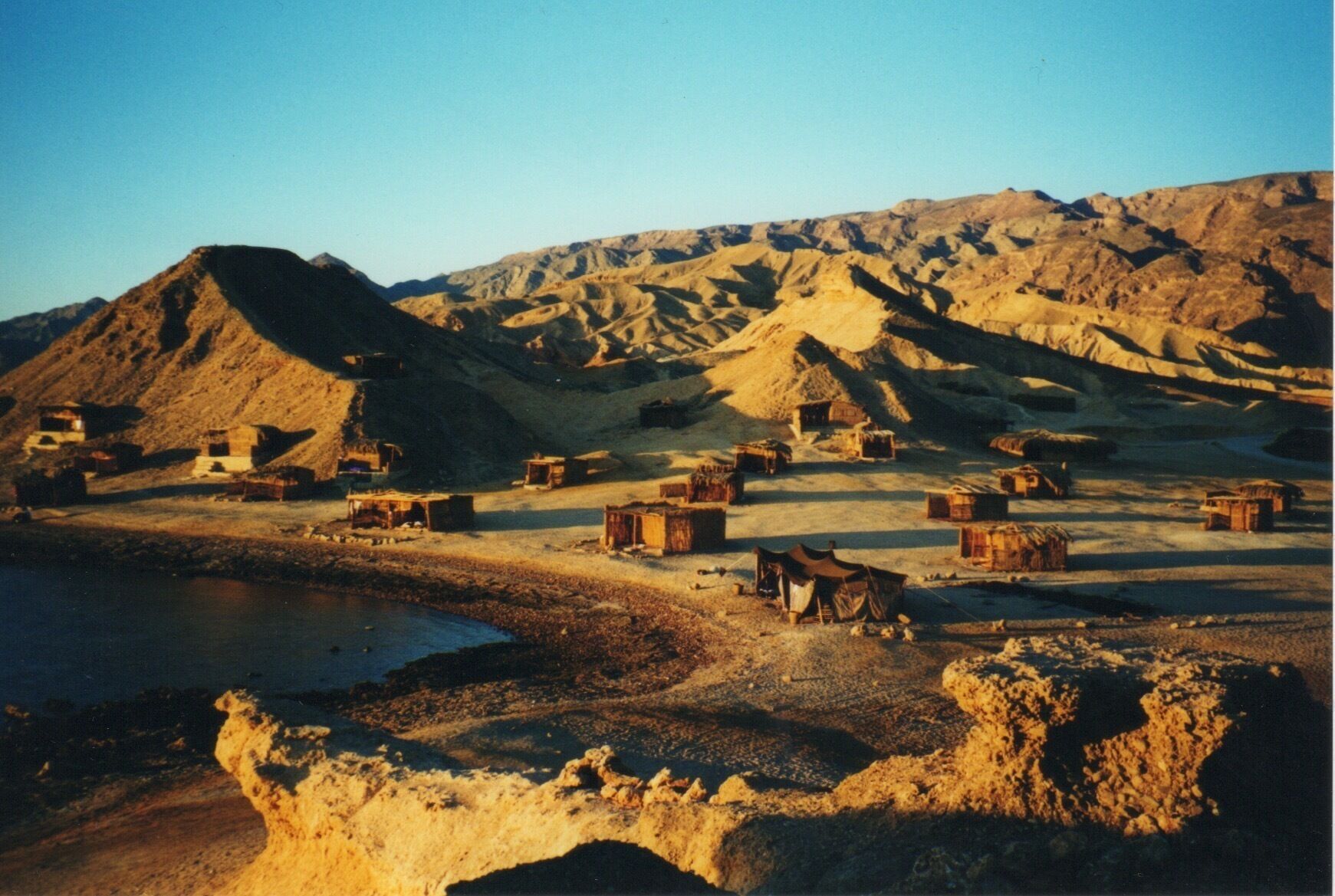 A desert landscape with scattered traditional huts and a large mountain in the background.