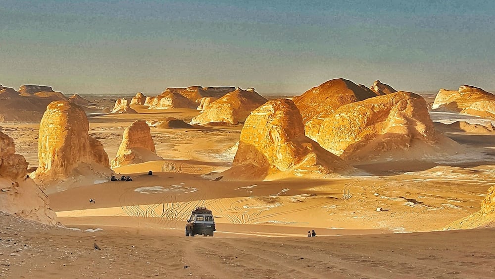 A desert landscape with prominent rock formations and a vehicle on a dirt road.