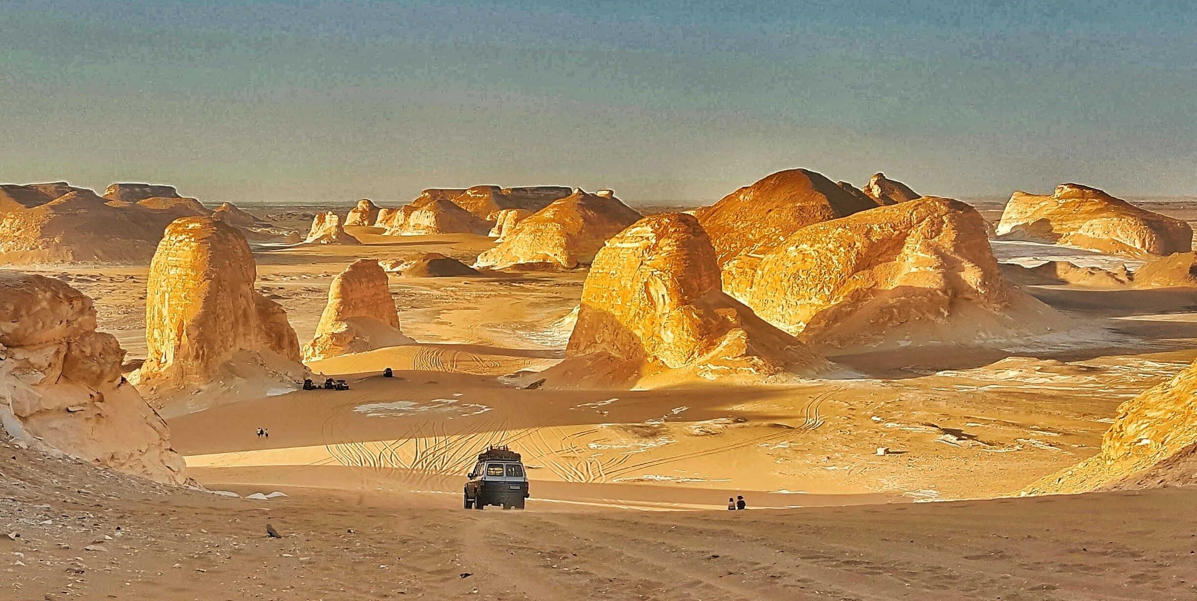 A desert landscape with prominent rock formations and a vehicle on a dirt road.