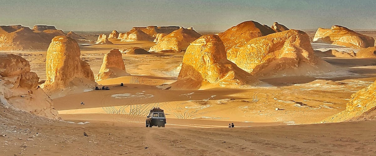 A desert landscape with prominent rock formations and a vehicle on a dirt road.