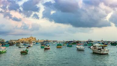 ALEXANDRIA, EGYPT - NOVEMBER 20, 2016: Cityscape with egyptian fisher boats, vessels and ships in the seaport at sunrise. Panoramic view with Qaitbay Citadel in a harbour of Alexandria.
