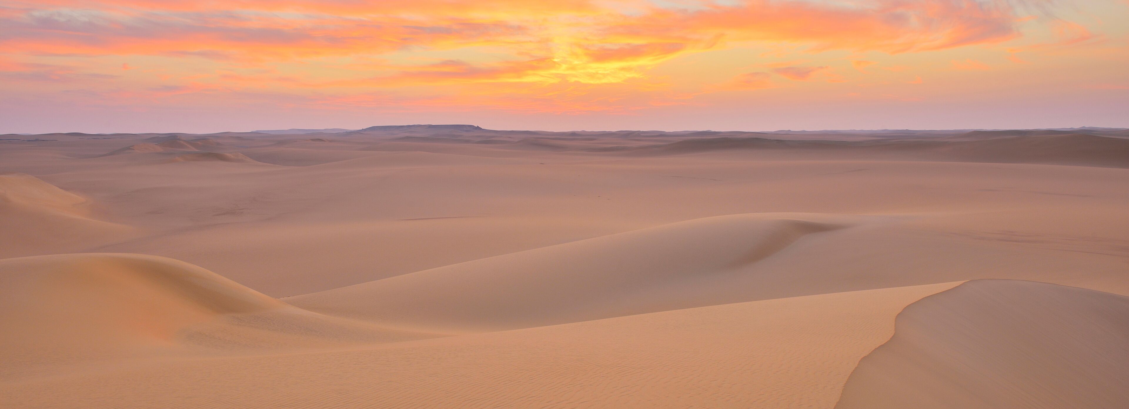 A desert landscape with rolling sand dunes under a sunset sky.