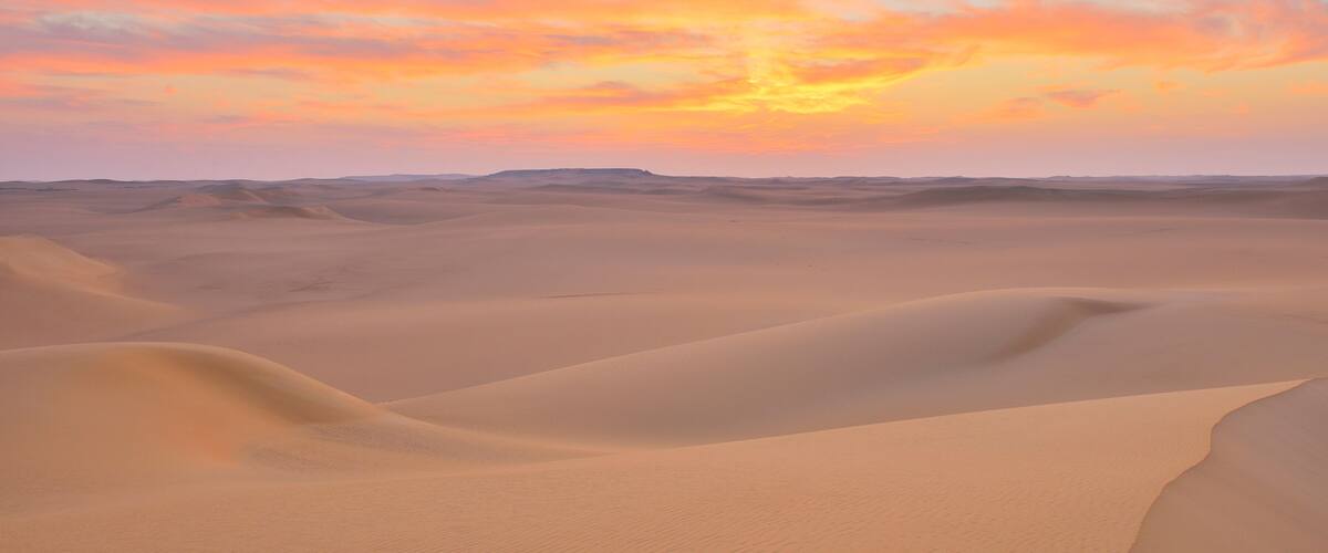A desert landscape with rolling sand dunes under a sunset sky.
