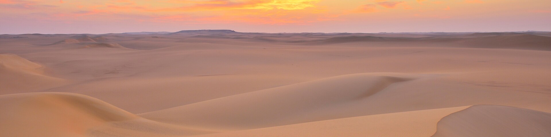 A desert landscape with rolling sand dunes under a sunset sky.