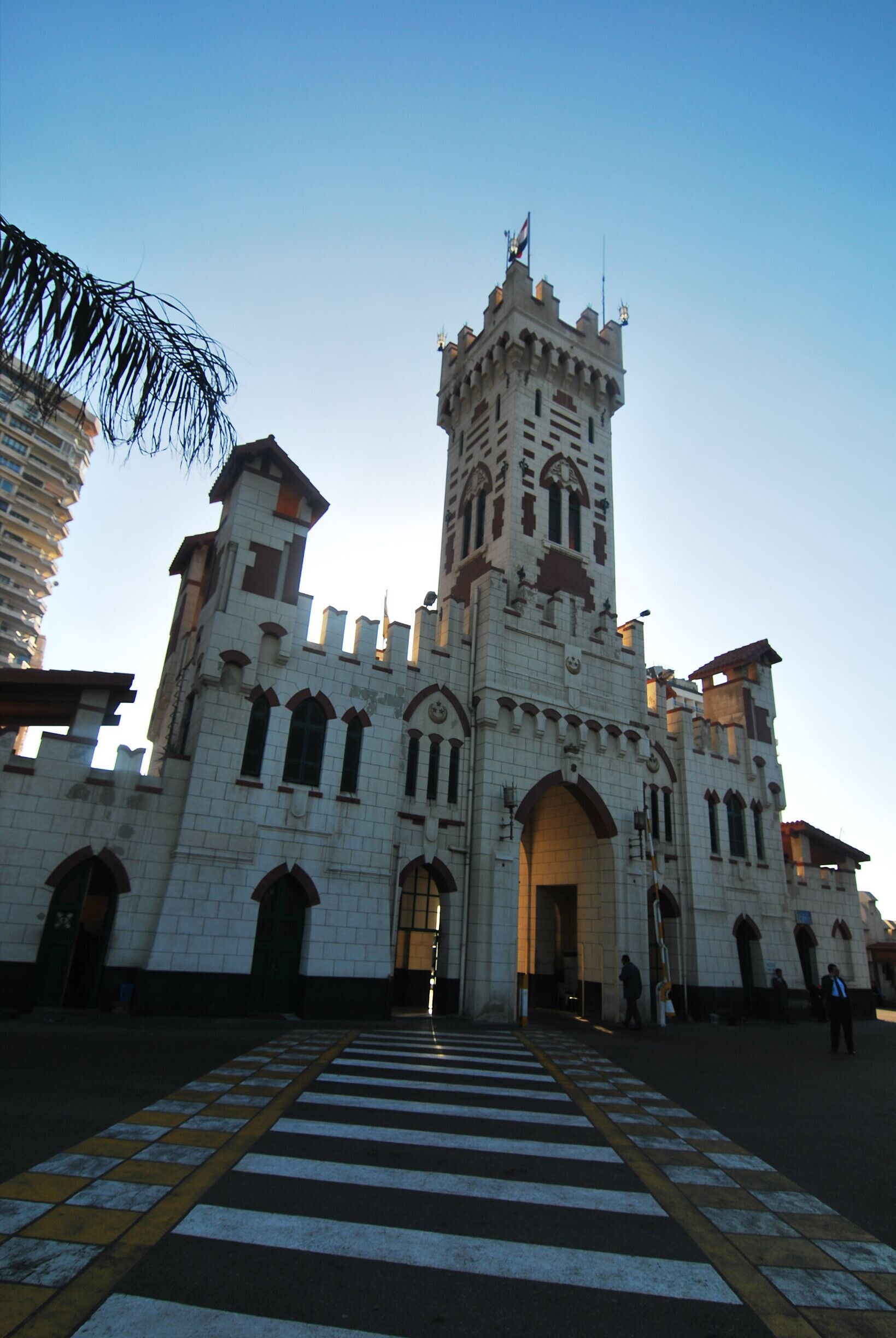 A large castle-like building with a tall tower, arched windows, and a flag on top.