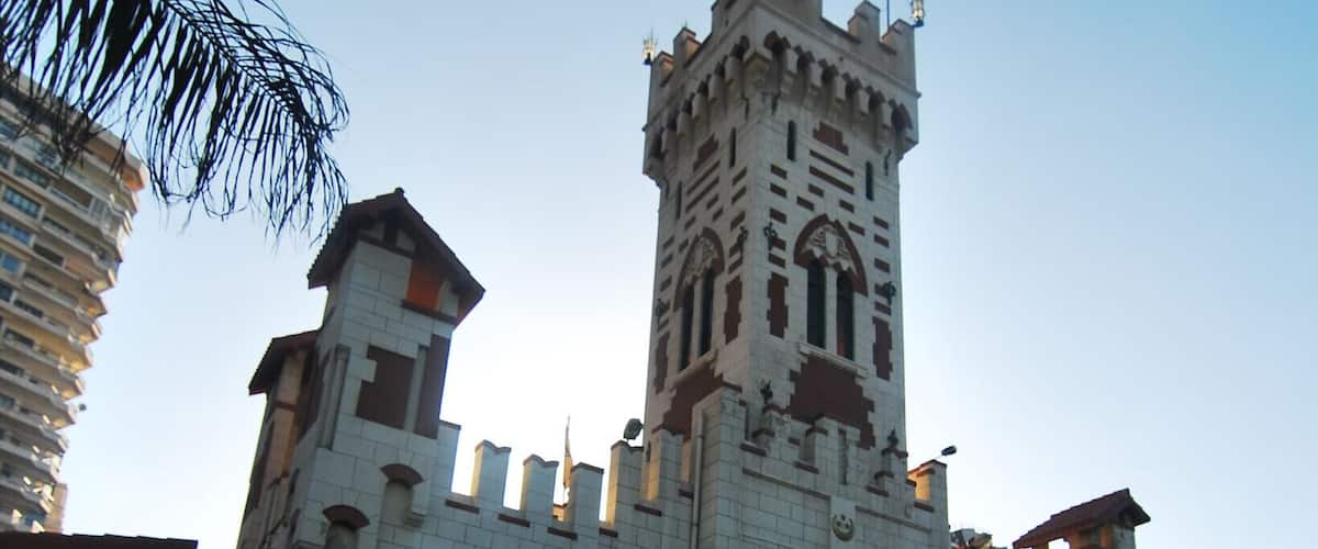 A large castle-like building with a tall tower, arched windows, and a flag on top.