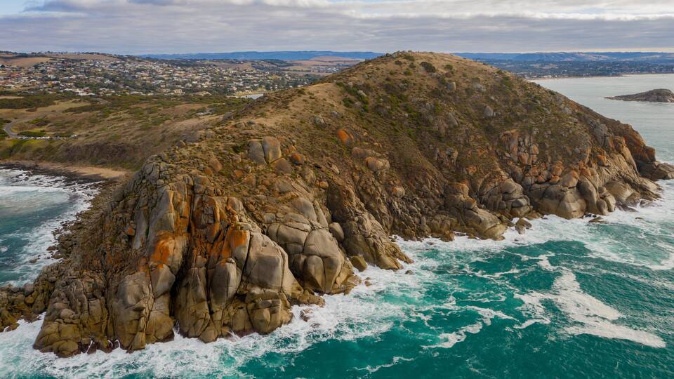 A rocky coastal landscape with a prominent hill and a view of a town in the background.