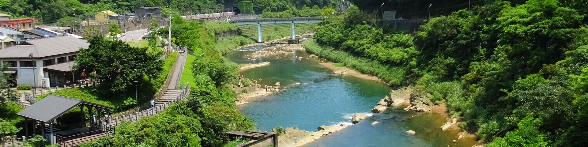 A river flowing through a valley with lush greenery and a bridge in the distance.