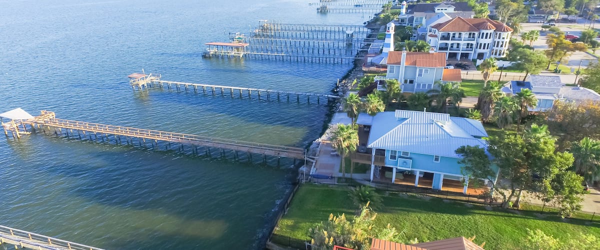 Aerial view three-story waterfront vacation home with fishing piers stretching out over the Galveston Bay in Kemah city, Texas, USA. Bird eye view of Kemah Lighthouse District at sunset.