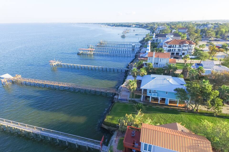 A coastal residential area with a pier extending into the water, surrounded by houses and palm trees.