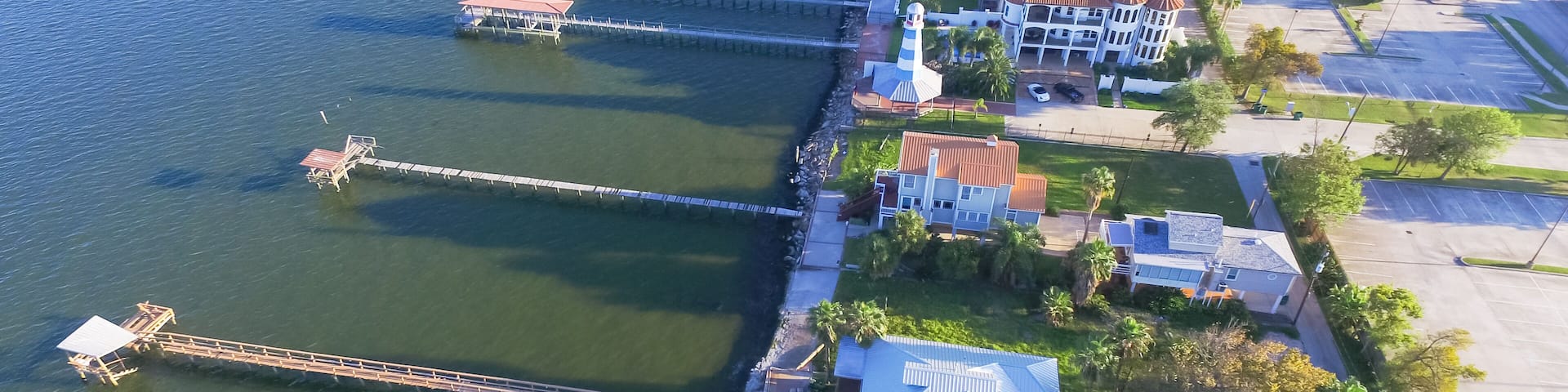 Aerial view three-story waterfront vacation home with fishing piers stretching out over the Galveston Bay in Kemah city, Texas, USA. Bird eye view of Kemah Lighthouse District at sunset.