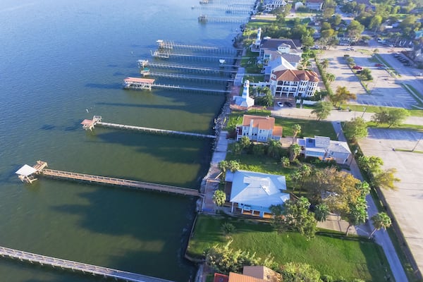 Aerial view three-story waterfront vacation home with fishing piers stretching out over the Galveston Bay in Kemah city, Texas, USA. Bird eye view of Kemah Lighthouse District at sunset.