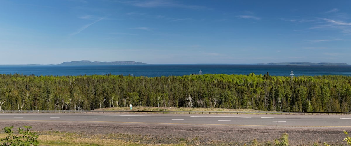 A highway with a forested area and a distant view of the ocean.