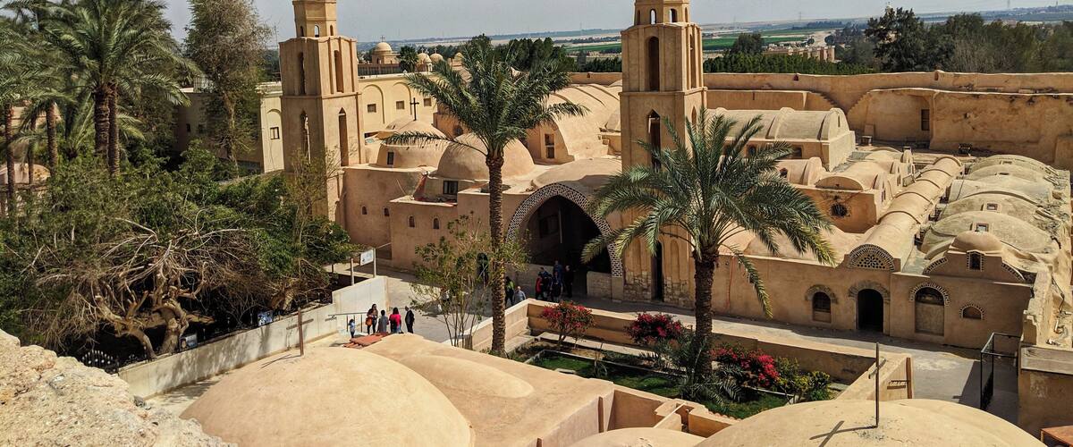 A historic walled city with traditional architecture, palm trees, and a clear sky.