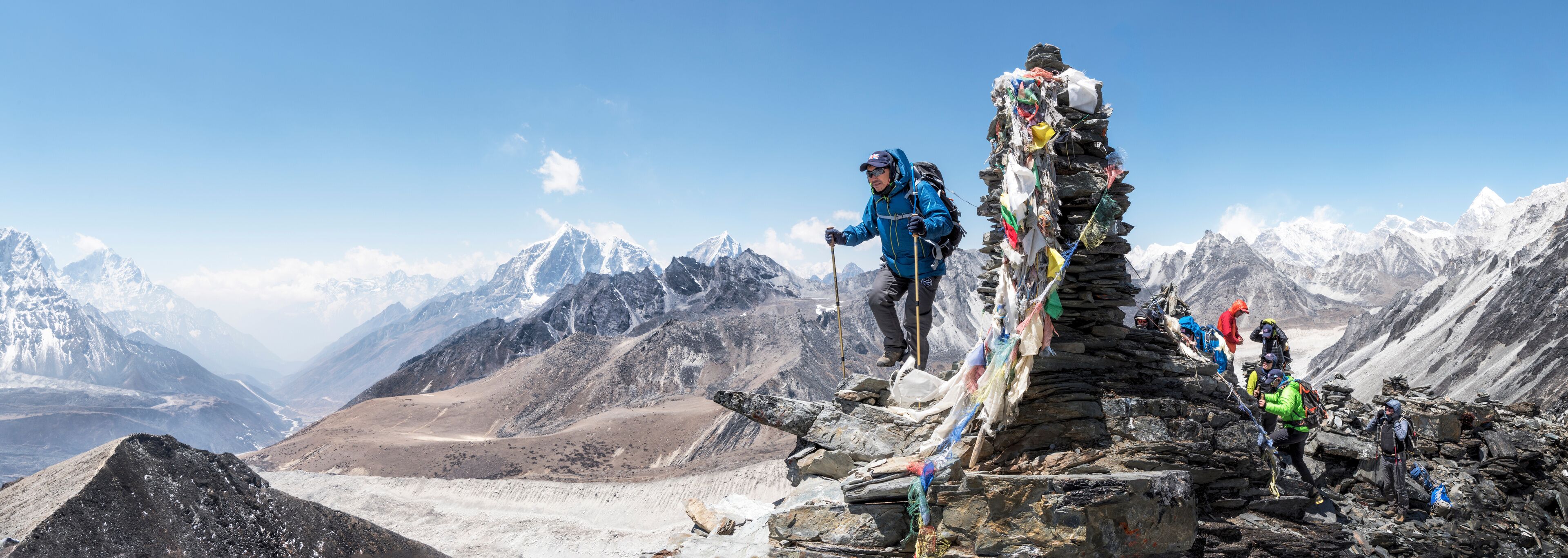 A group of climbers on a mountain peak with snow-covered peaks in the background.