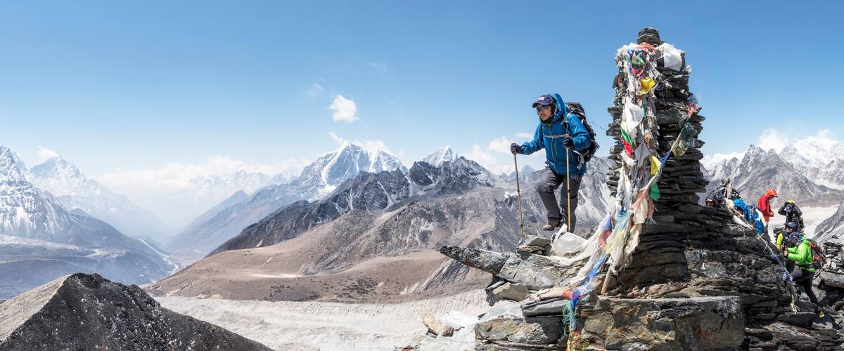 A group of climbers on a mountain peak with snow-covered peaks in the background.