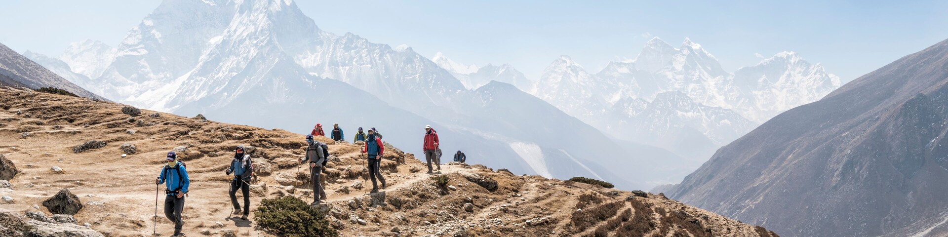 Um grupo de caminhantes numa trilha montanhosa, com picos nevados ao fundo.