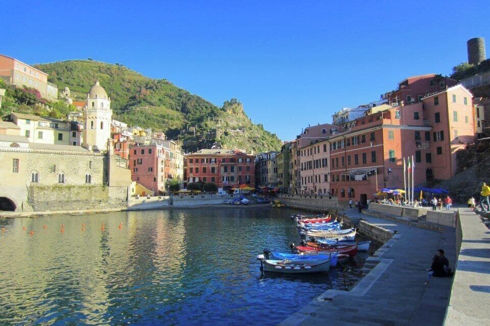 A coastal town with colorful buildings, a historic tower, and boats docked along the waterfront.