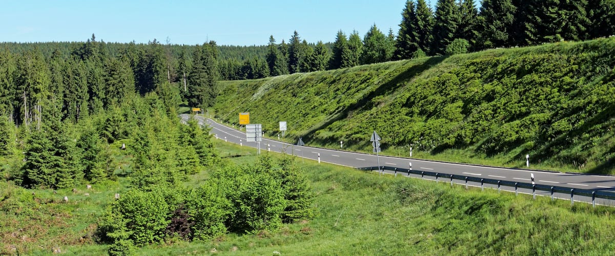 A highway curving through a forested area with a guardrail and road signs.