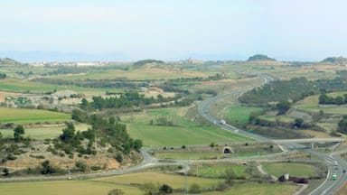 Uma estrada sinuosa serpenteia por uma paisagem ondulada, com campos e edifícios dispersos.