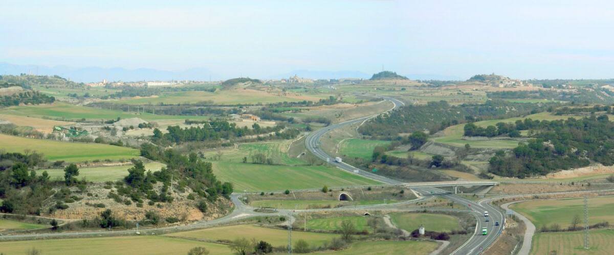 A winding road through a hilly landscape with fields and scattered buildings.