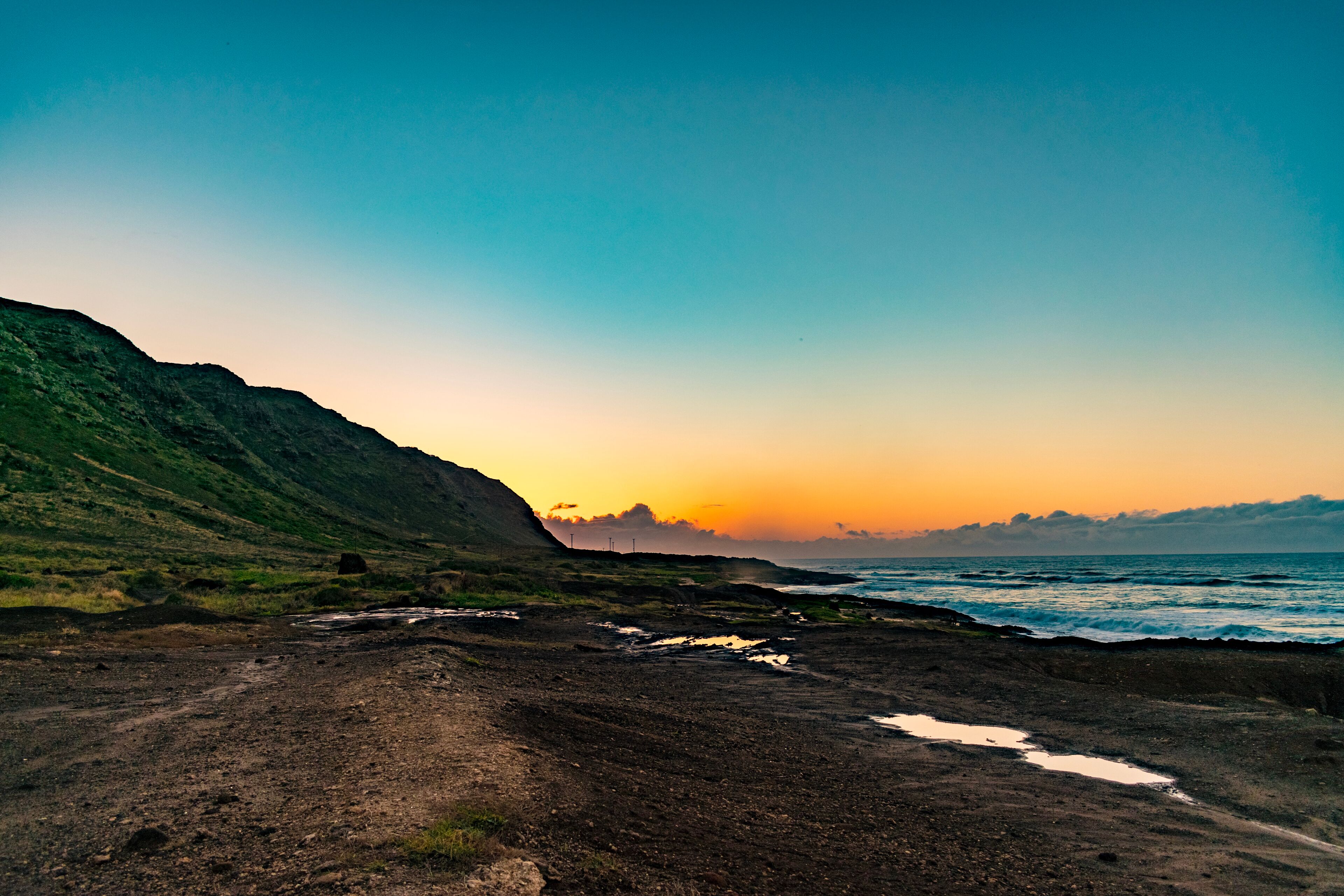 A coastal landscape with a dirt path, rocky terrain, and a body of water.