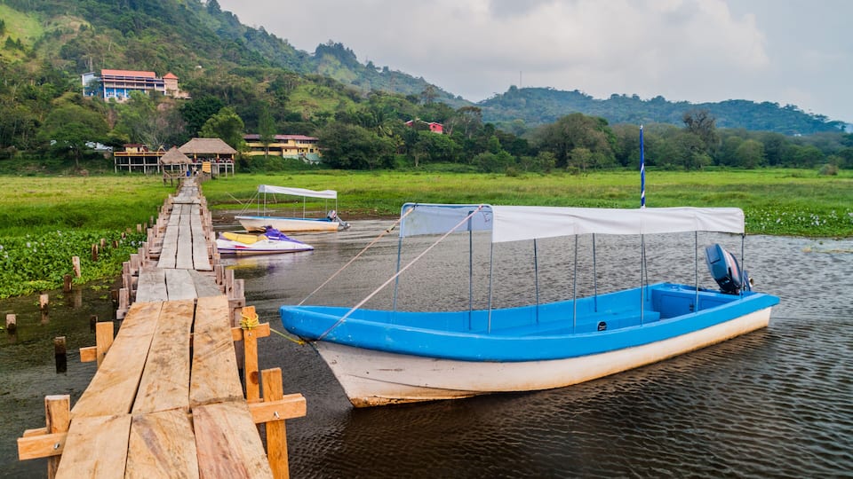 A wooden dock leading to a calm lake with boats.