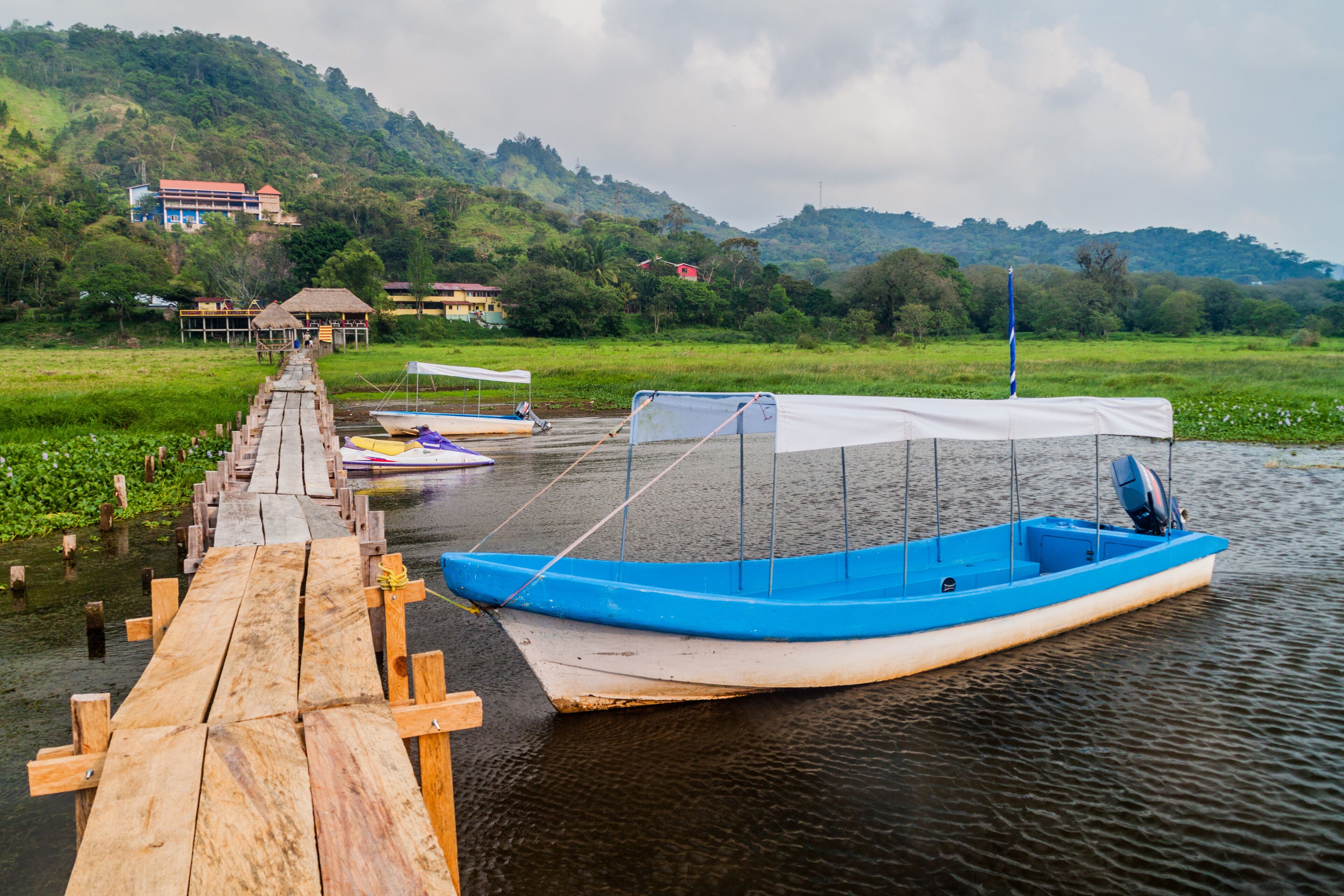 A wooden dock leading to a calm lake with boats.
