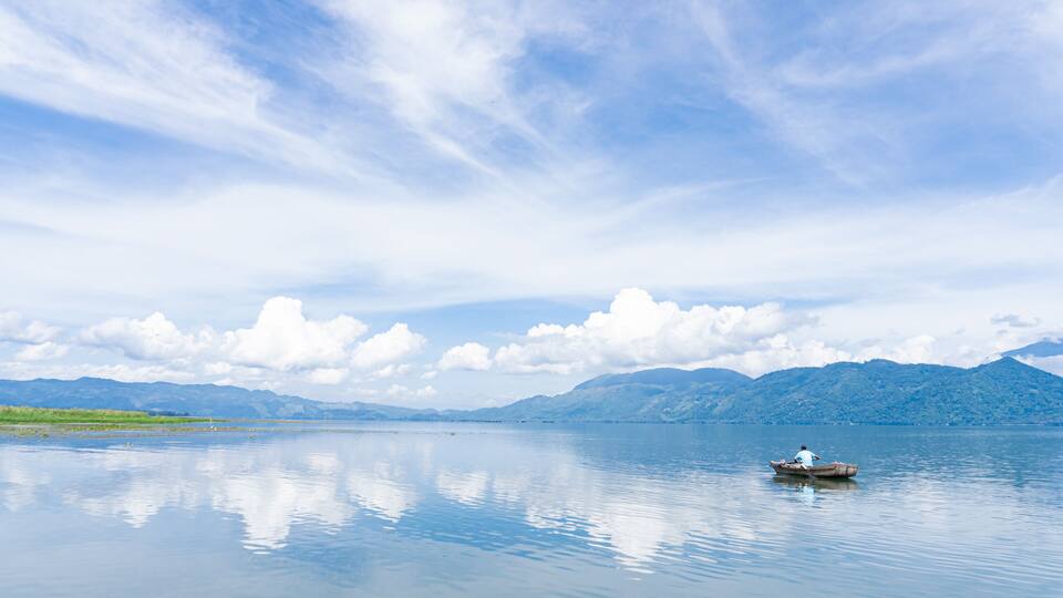 A calm lake with a small boat and mountains in the background.