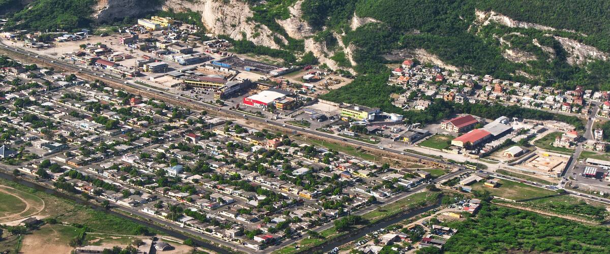 An aerial view of a town with a railway line, industrial buildings, and a mountainous backdrop.