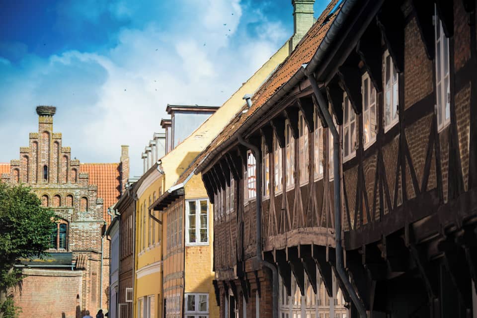 A historic street with timber-framed buildings and a prominent brick church in the background.