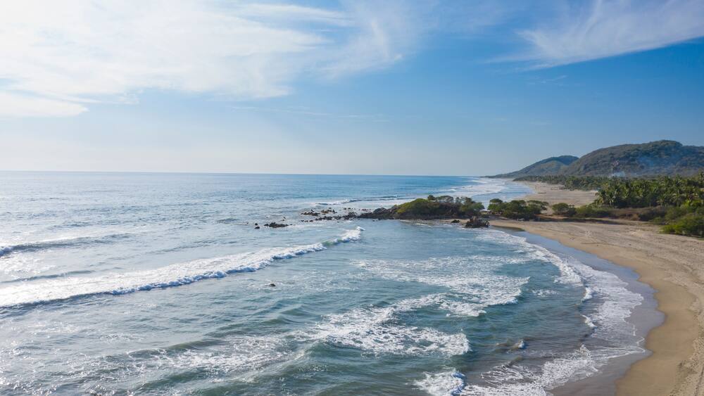 A beach with waves, a sandy shore, and a mountain in the background.