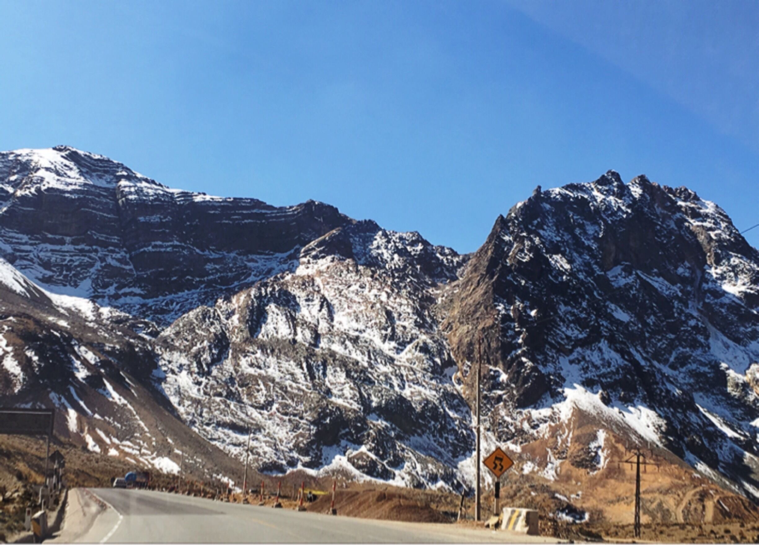 A snow-covered mountain range with a winding road and a warning sign.
