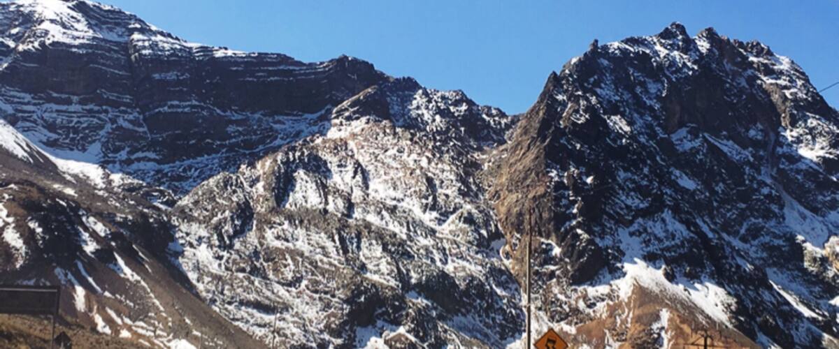 A snow-covered mountain range with a winding road and a warning sign.