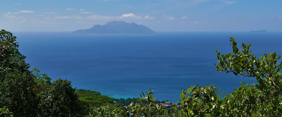 Panoramic view from Dans Gallas hiking trail in the north of Mahe, Seychelles over the northern coastline with the silhouettes of Silhouette Island and Ile du Nord on the horizon.