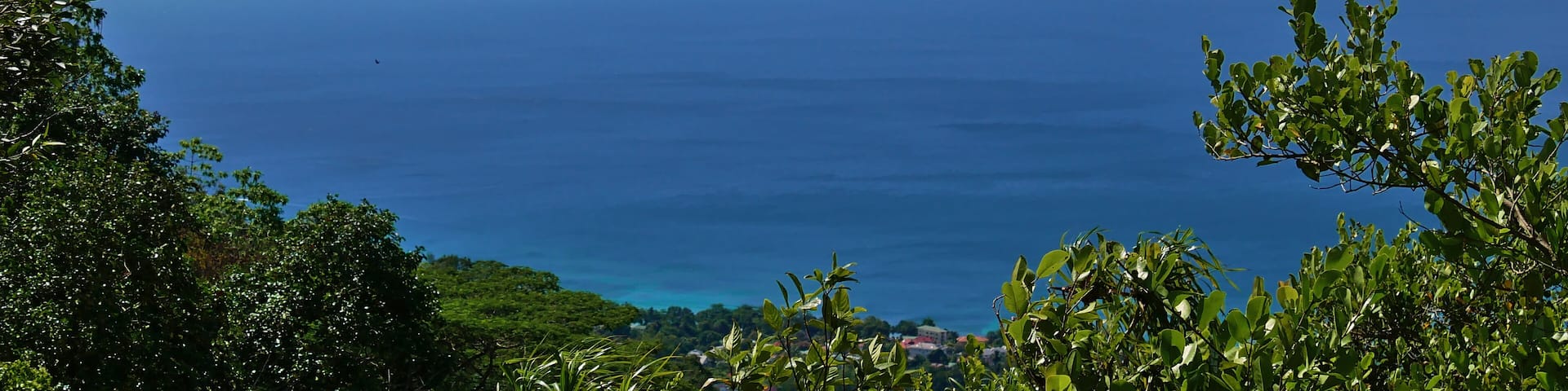 Panoramic view from Dans Gallas hiking trail in the north of Mahe, Seychelles over the northern coastline with the silhouettes of Silhouette Island and Ile du Nord on the horizon.