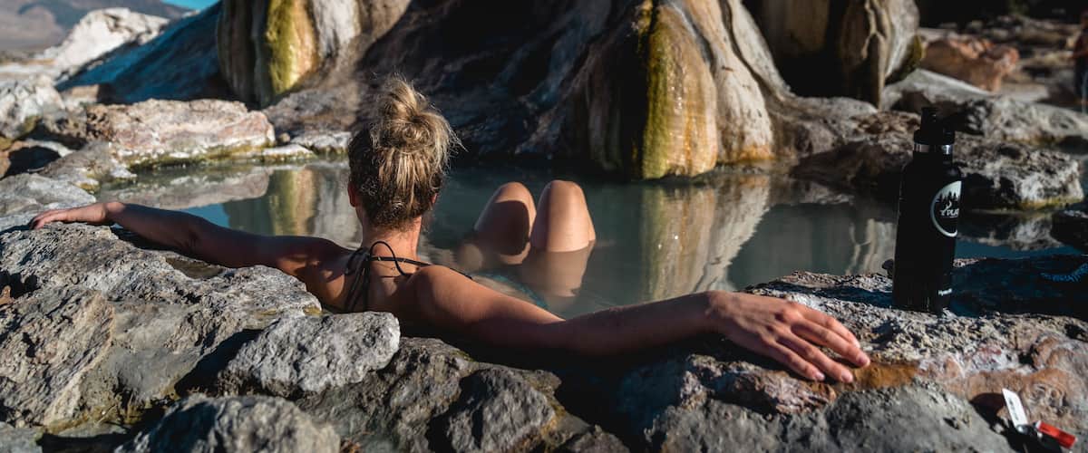 A person relaxing in a natural hot spring surrounded by large rocks.