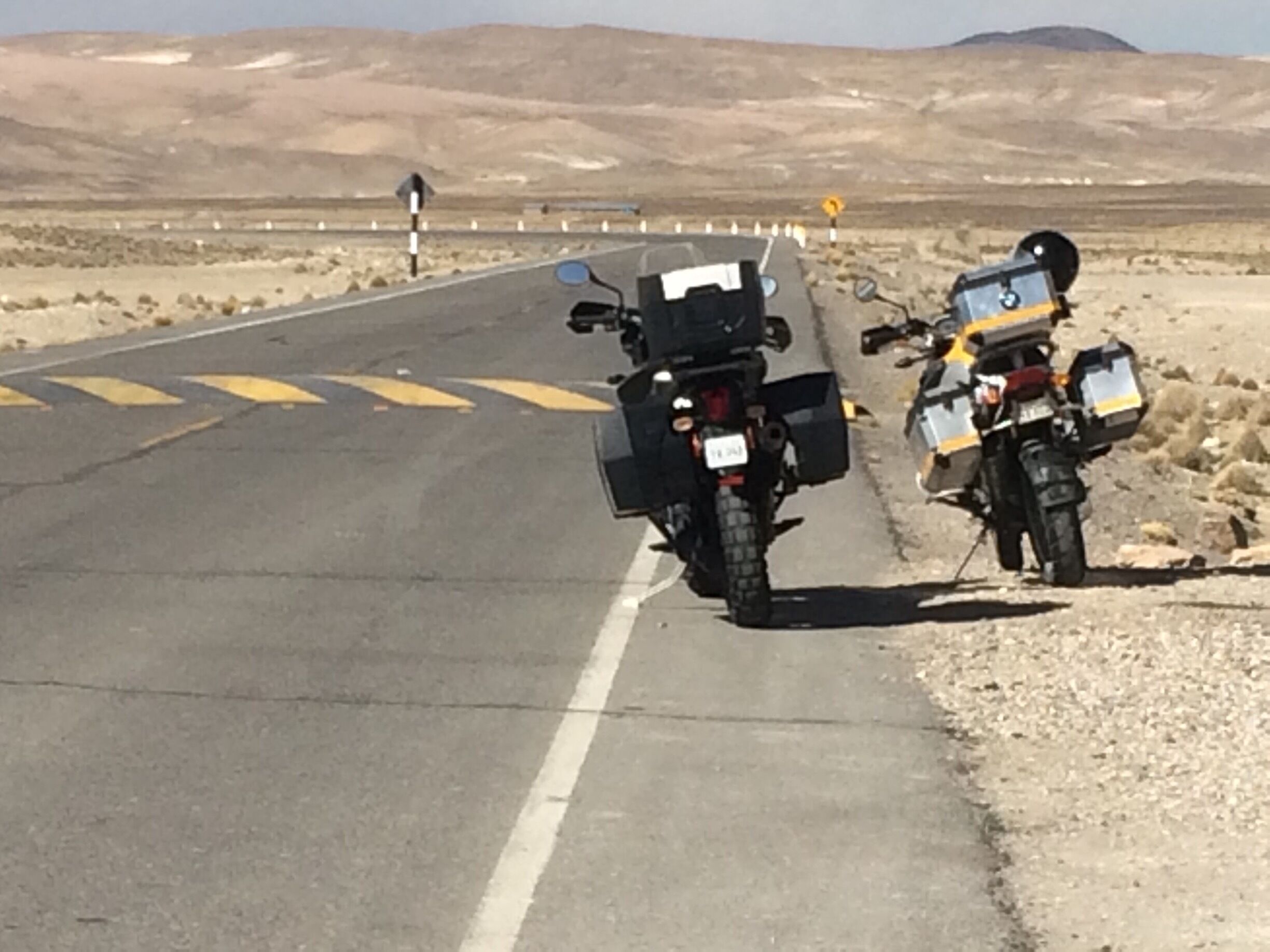 Two motorcycles parked on a road with desert scenery in the background.