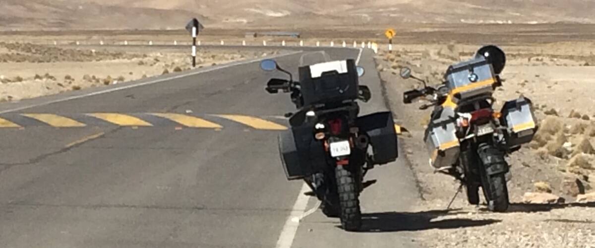 Two motorcycles parked on a road with desert scenery in the background.