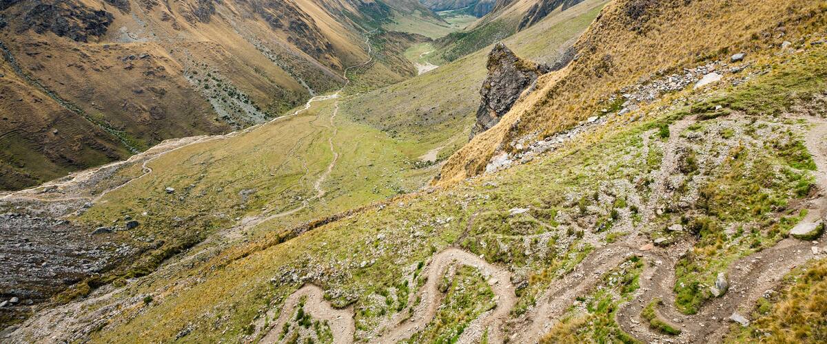 A mountain valley with a winding path, rocky terrain, and a river.