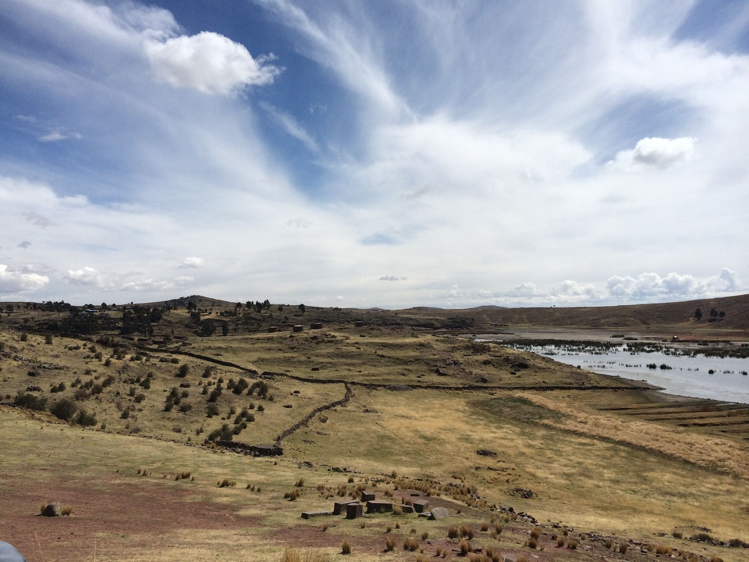 A rural landscape with rolling hills, a small body of water, and scattered buildings.