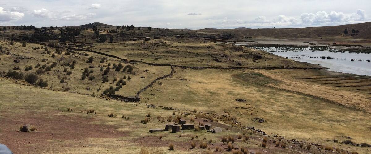 A rural landscape with rolling hills, a small body of water, and scattered buildings.
