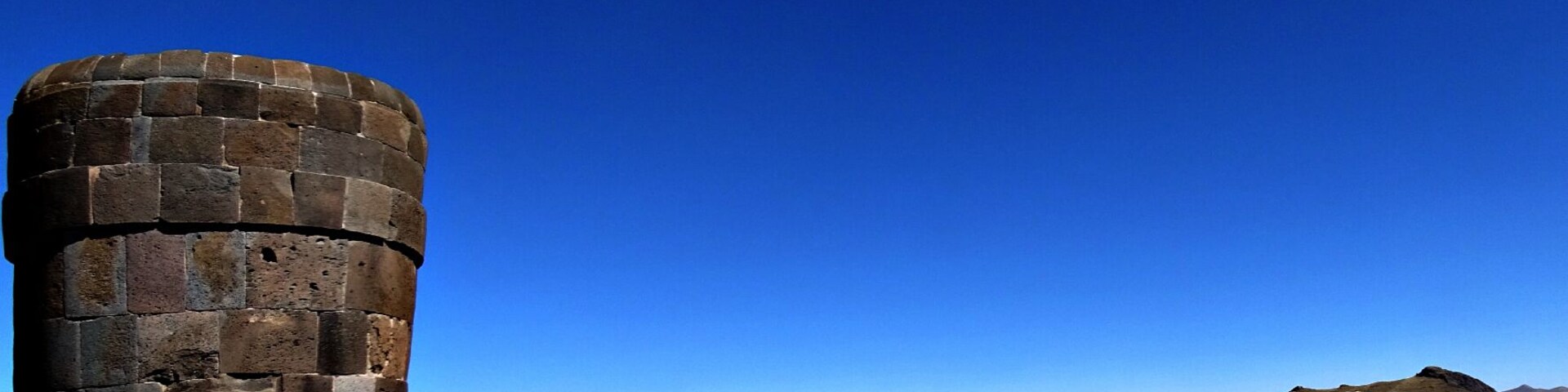Uma torre de pedra à beira de um lago, com um céu azul límpido.